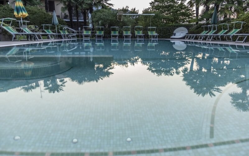 Serene pool scene with reflections, surrounded by lounge chairs, umbrellas, and lush greenery, evoking tranquility.