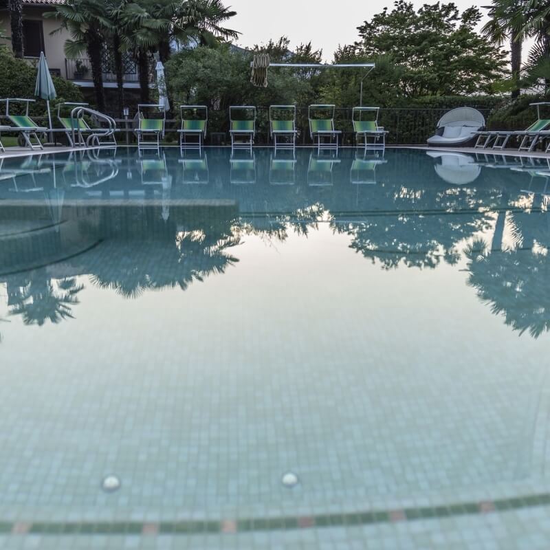 A serene pool scene with light blue water, red accent tiles, white lounge chairs, and a charming building in the background.