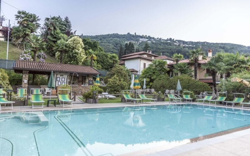 Serene pool scene with lounge chairs, umbrellas, a hot tub, and lush greenery, creating a tranquil atmosphere.