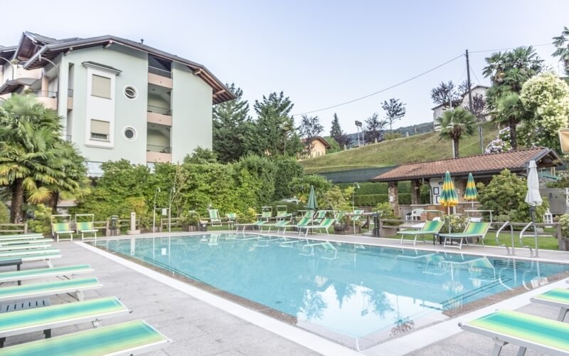 Serene pool scene with lounge chairs, umbrellas, a sloping roof building, and a hillside under a clear sky.