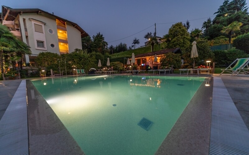 Serene hotel pool area with teal water, lounge chairs, umbrellas, and lush greenery under a clear blue sky.