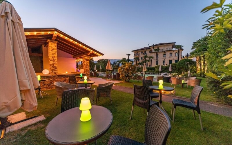 Serene outdoor hotel setting with a grassy lawn, cozy seating, warm lighting, and a pool surrounded by lush greenery.