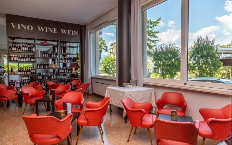 Restaurant dining area with wine display, white and brown walls, red leather chairs, and large windows with outdoor views.