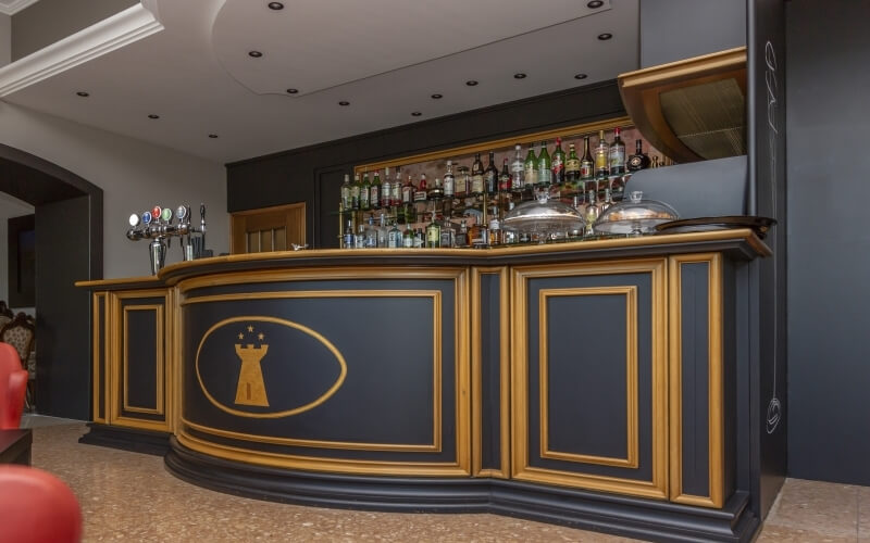 Elegant bar with a black and gold counter, liquor bottles on display, and a dimly lit doorway in the background.