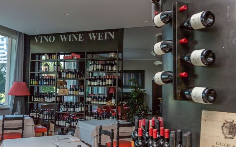 Cozy wine shop with shelves of wine bottles, a dining area, and natural light, creating an inviting atmosphere.