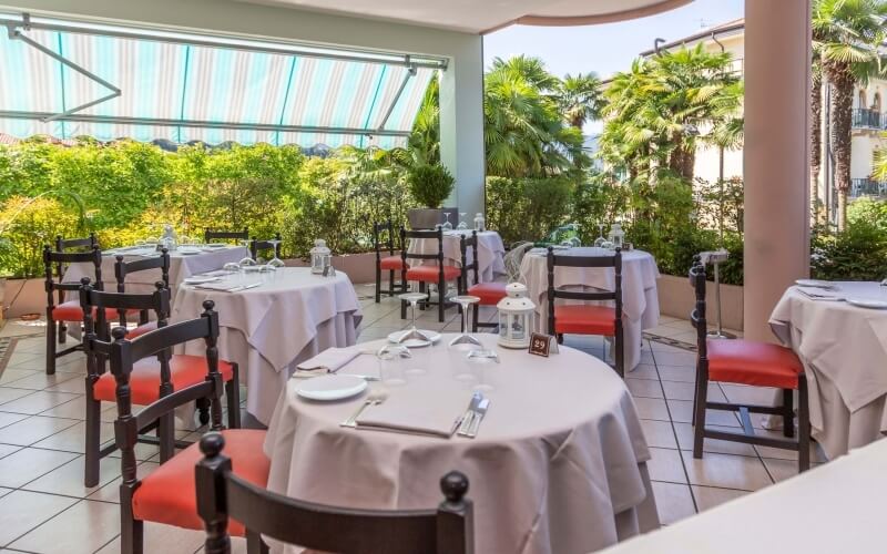 Serene outdoor dining area with elegant tables, lush greenery, and warm lantern lighting under a striped awning.