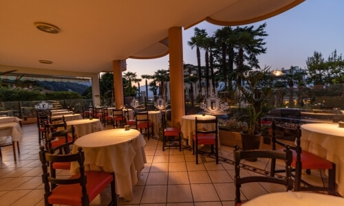 Tranquil dining area at dusk with round tables, ocean views, lush gardens, and a curved awning on an elevated patio.