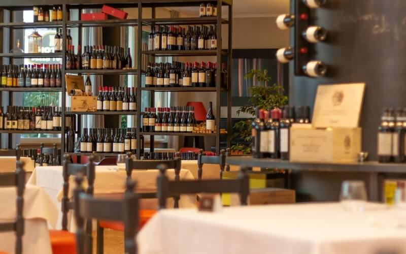 A sophisticated wine bar with shelves of wine bottles, elegant tables, and natural light creating a warm atmosphere.