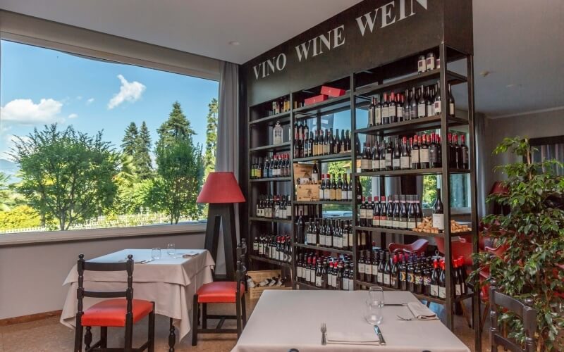 Restaurant interior with two tables, wine display, and a view of a tree and blue sky through a large window.