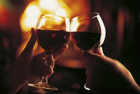 Two hands raise wine glasses in a toast against a dark background, creating an intimate and celebratory atmosphere.