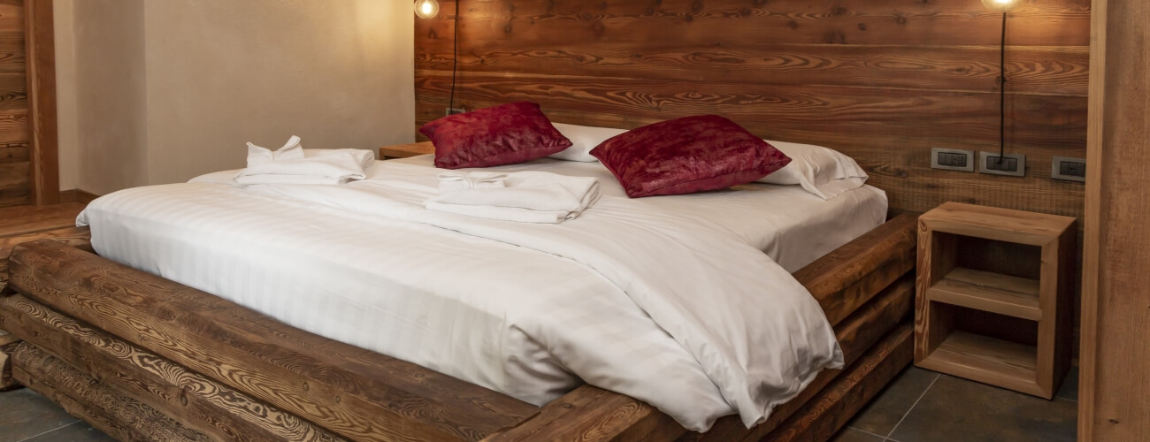 Serene bedroom with a double bed, red and white pillows, wooden nightstand, and warm beige walls, exuding tranquility.