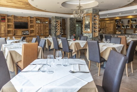 Upscale restaurant dining room with recessed lighting, a circular accent light, wooden shelves, and wine bottles on display.