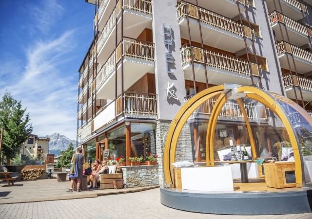 Edificio multi-piano con facciata in pietra grigia, insegna "L'ETAGE" e area esterna con struttura a cupola in legno e vetro.
