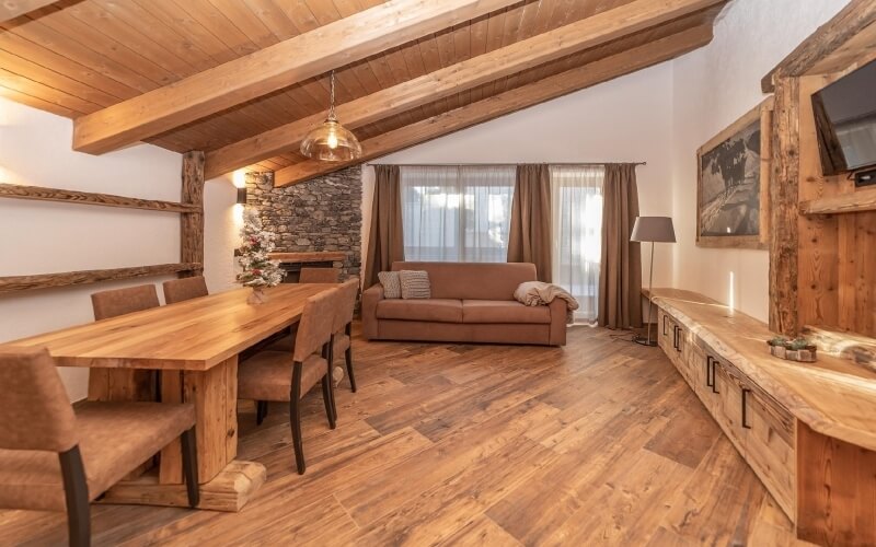 Rustic open-plan living space with a dining area, seating zone, wooden beams, and a cozy fireplace.
