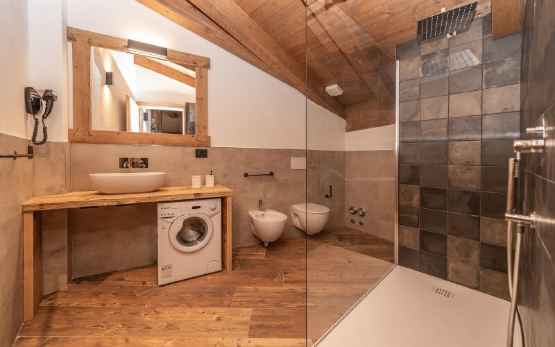 Bagno con elementi moderni e rustici, lavabo su un piano in legno, bidet, doccia con parete in vetro e soffitto in legno.