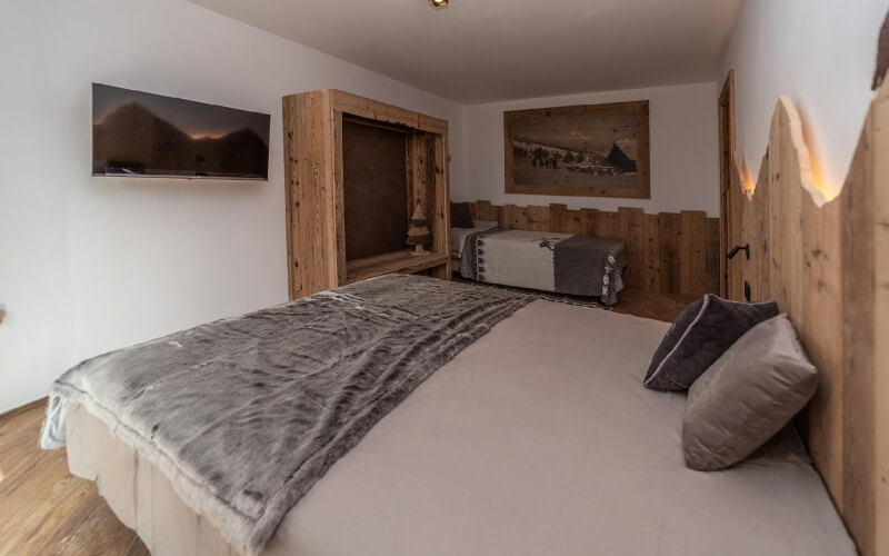 Camera da letto accogliente con due letti, TV, dipinto, pareti bianche e pavimenti in legno. Atmosfera invitante e ordinata.