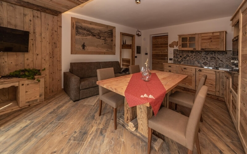 Cozy rustic living room and kitchen with wooden dining table, brown couch, and warm decor, exuding comfort and warmth.