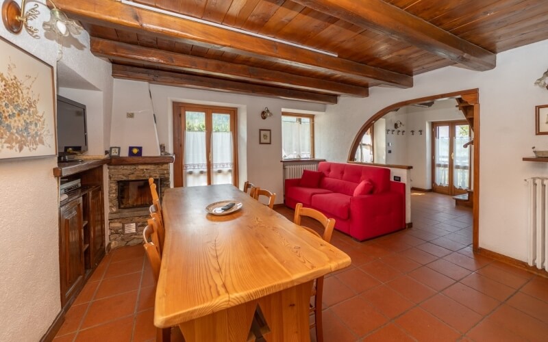 Cozy living room with dining area, wooden table, red couch, fireplace, and white walls with red tiled floor.