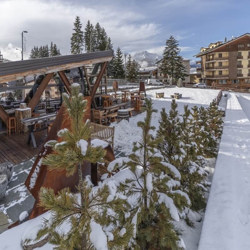 Area esterna con tavoli e sedie di legno coperti di neve.