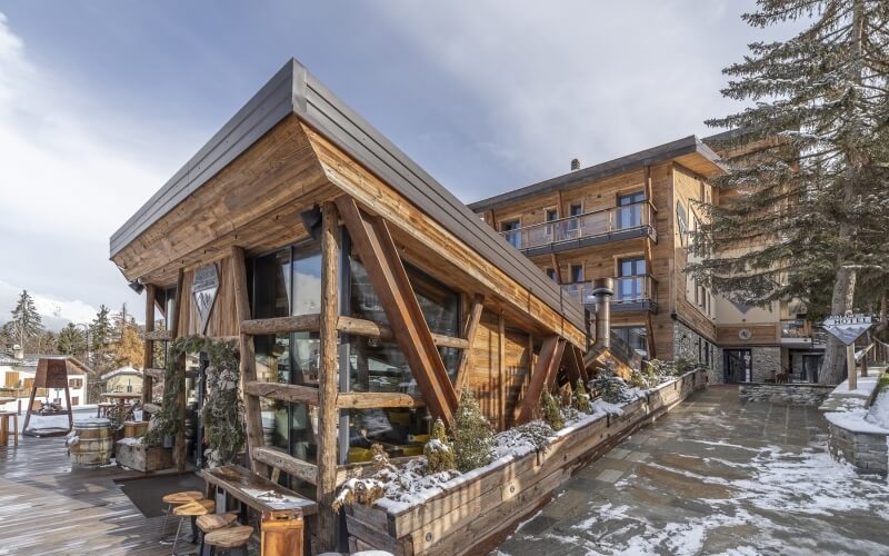 Hotel con facciata in legno, neve e area bar visibile.