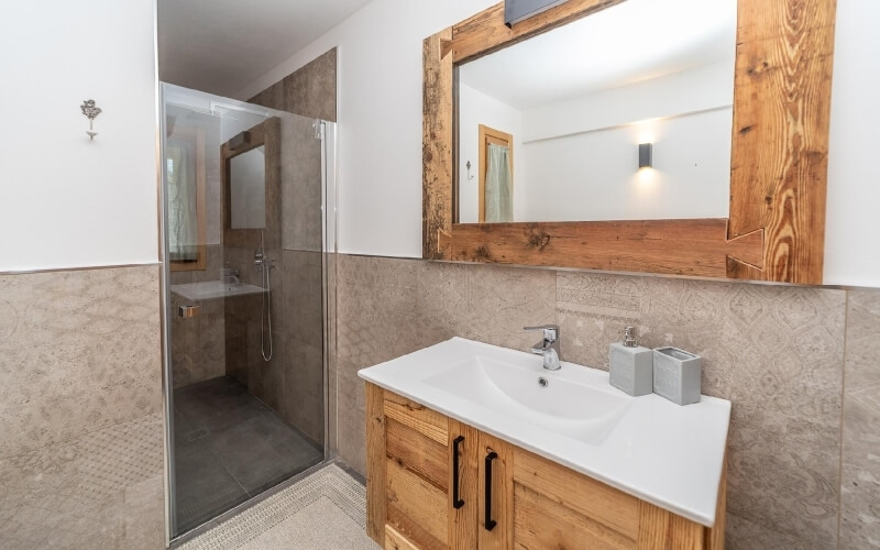 Bagno moderno con doccia in vetro, lavabo con piano bianco, specchio in legno e pavimento con tappeto beige.
