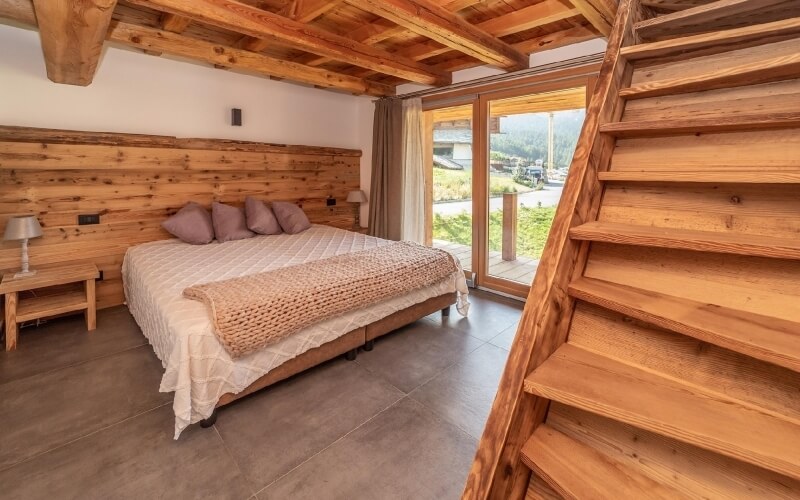 Camera da letto serena con letto, comodino, lampada e scala in legno che porta a un'area esterna con prato e patio.