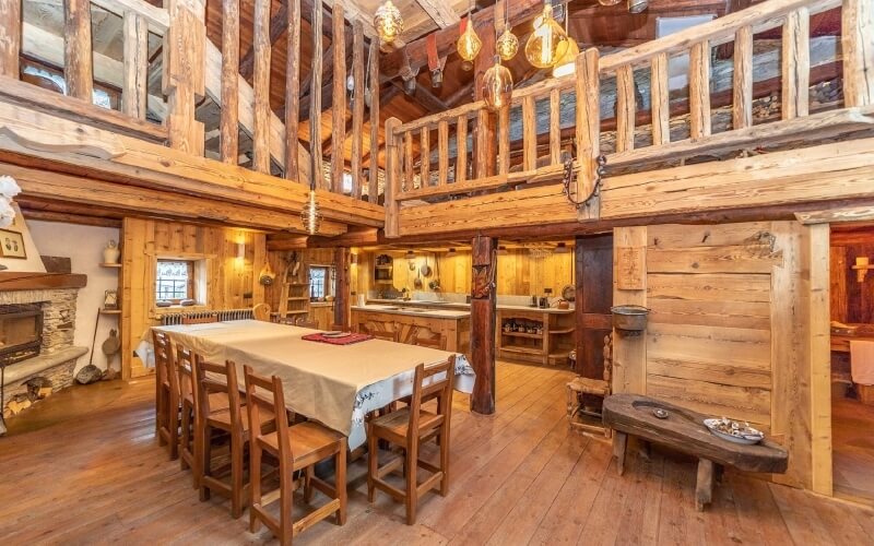 Cozy interior with exposed beams, stone fireplace, loft area, large dining table, and rustic kitchen.