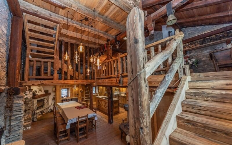 Two-story log cabin with a staircase, dining area on the first floor, and a loft overlooking the space. Cozy atmosphere.