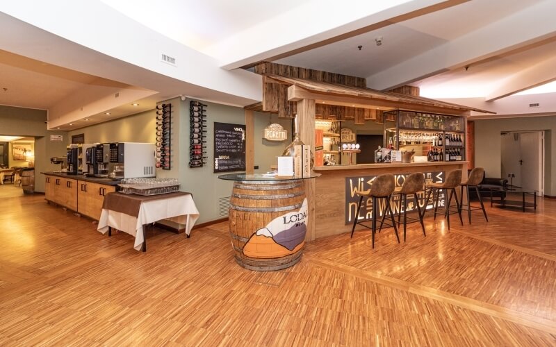 Cozy bar and kitchen area in a well-lit room with wooden floors, a large barrel, and shelves of wine bottles.