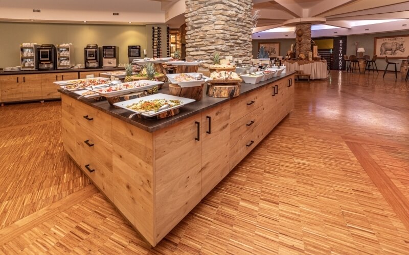 Spacious buffet restaurant with stone wall, large food island, wooden floor, green wall, and inviting dining area.