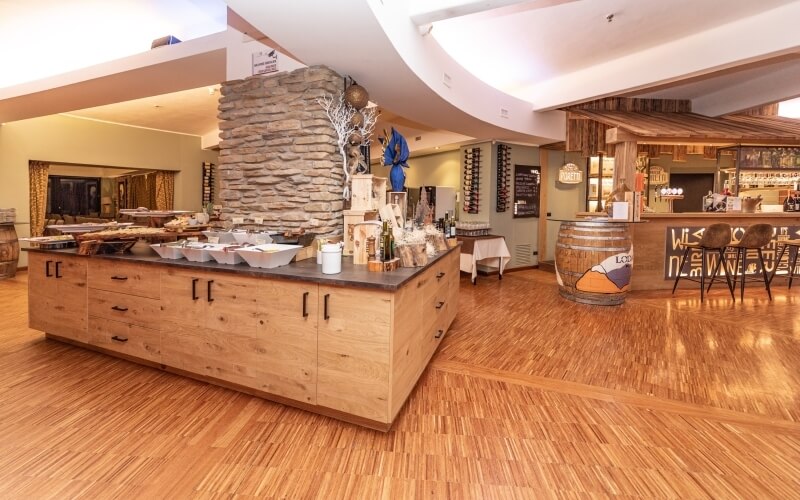 Modern restaurant interior featuring a large wooden kitchen island, bar, wine racks, and a cozy log fire.