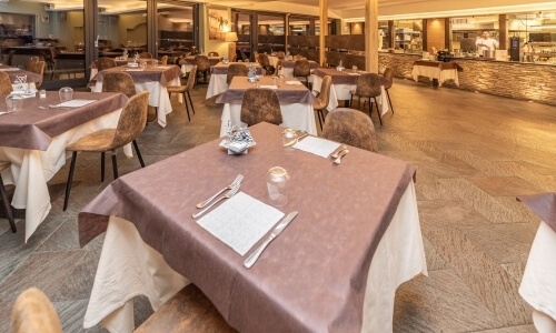 Spacious restaurant dining area with elegant tables, leather chairs, and a stone wall separating the kitchen.