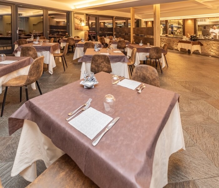 Ristorante elegante e vuoto con tavoli apparecchiati, cucina visibile e luce naturale che illumina l'ambiente.