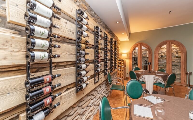 A cozy restaurant room with a wooden wine rack, tables set for dining, and an arched doorway leading to another space.