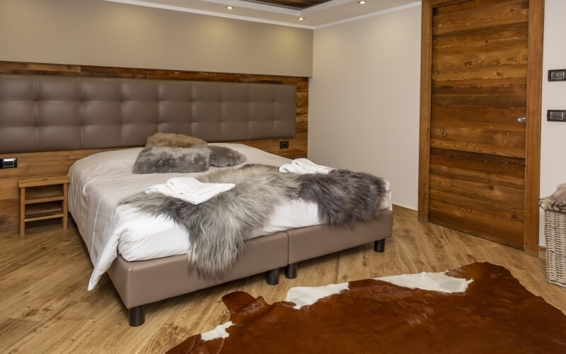 Cozy bedroom with a large bed, nightstand, wooden door, and cowhide rug, featuring a leather headboard and white comforter.