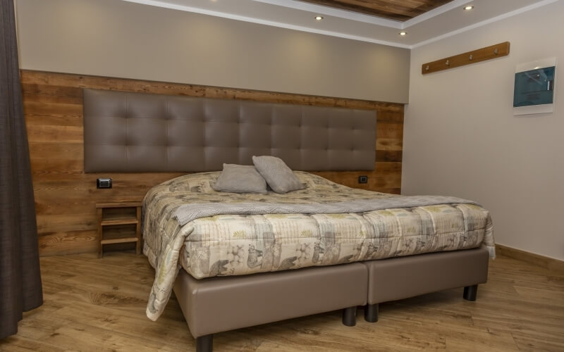 Cozy bedroom featuring a large bed with a leather headboard, gray pillows, and warm lighting, set on a wooden floor.