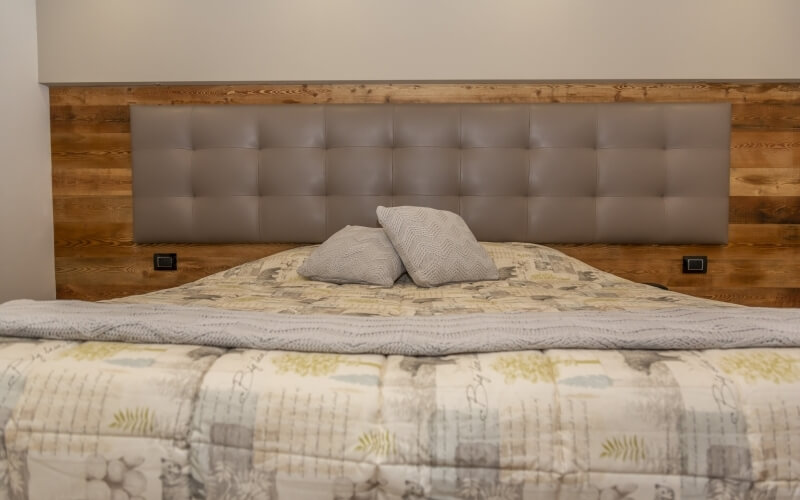 Serene bedroom with a wooden headboard, floral comforter, gray cushions, and light wood accents, creating a calm atmosphere.