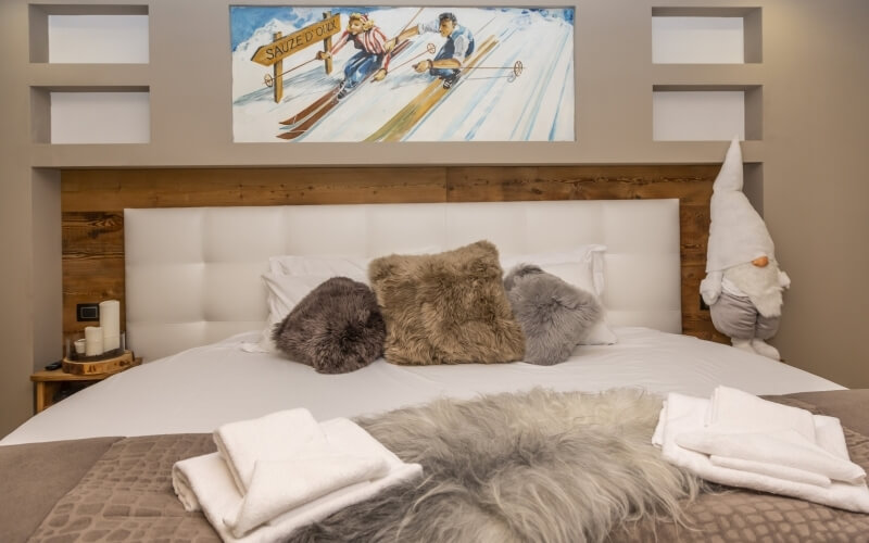 Serene bedroom with a white bed, brown and gray pillows, folded towels, and a vibrant skiing painting above.