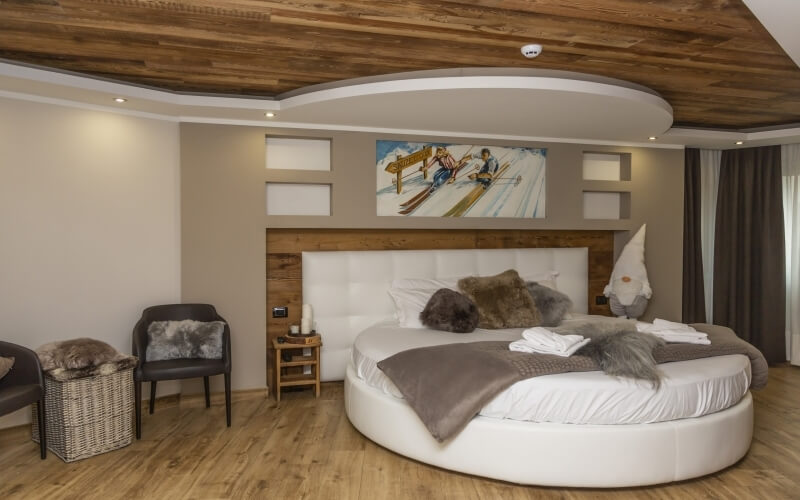 Modern bedroom featuring a circular bed, warm beige walls, dark wood ceiling, and whimsical skier painting.