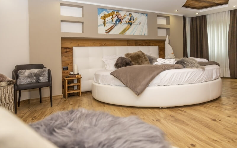 Modern bedroom with a circular bed, a skiing painting above, wooden nightstand, and cozy decor elements.