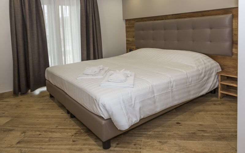 Minimalist hotel room with a bed, white duvet, leather headboard, and natural light from open curtains.