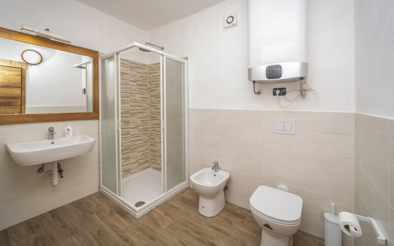 Bagno compatto con doccia in vetro, WC, bidet, lavabo e specchio, pavimento in legno e piastrelle, atmosfera pulita.