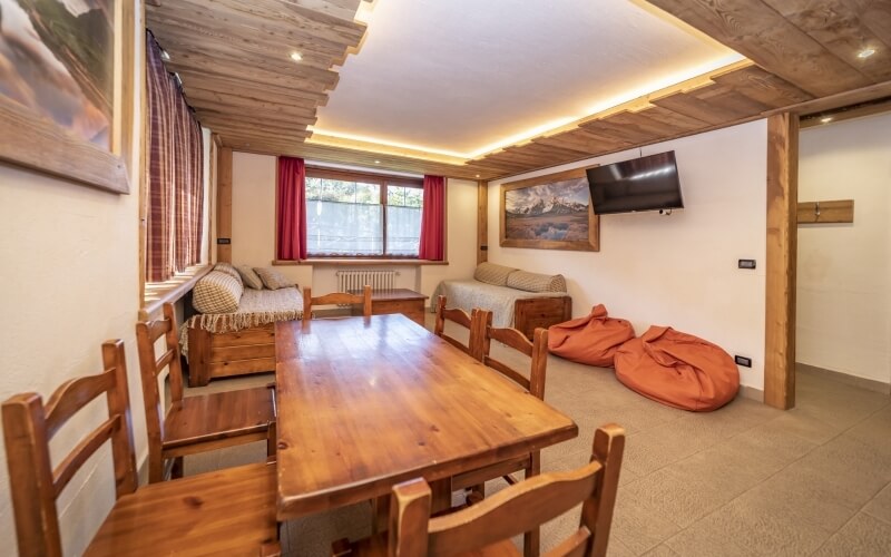 Interno di un soggiorno e sala da pranzo con tavolo di legno, sedie, divano, e grande finestra che illumina l'ambiente.