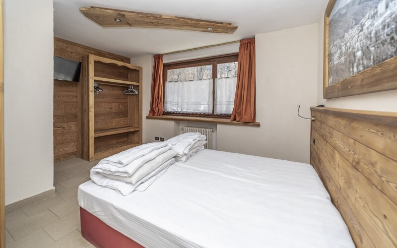 Una stanza accogliente con un letto, finestra, armadio e decorazioni calde.