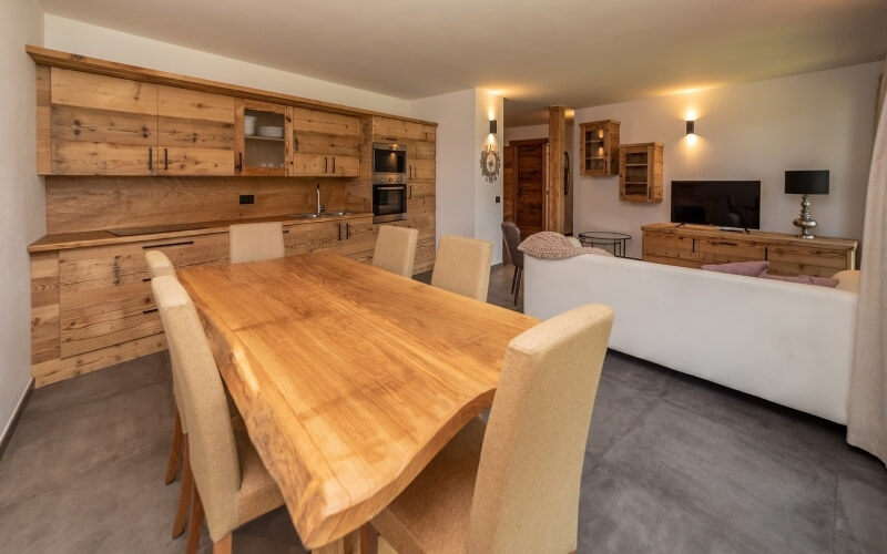 Spazio abitativo moderno e minimalista con cucina, tavolo da pranzo e soggiorno con divano e TV montata.