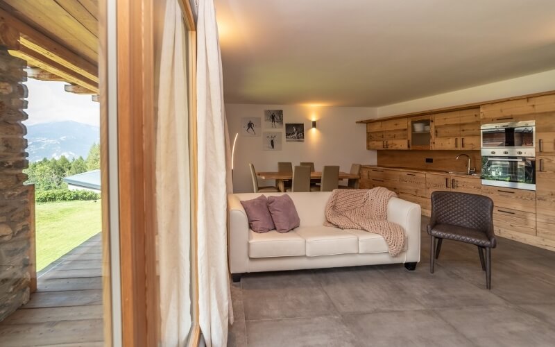 Una stanza luminosa con un divano bianco, un tavolo da pranzo in legno e un'area cucina a destra.