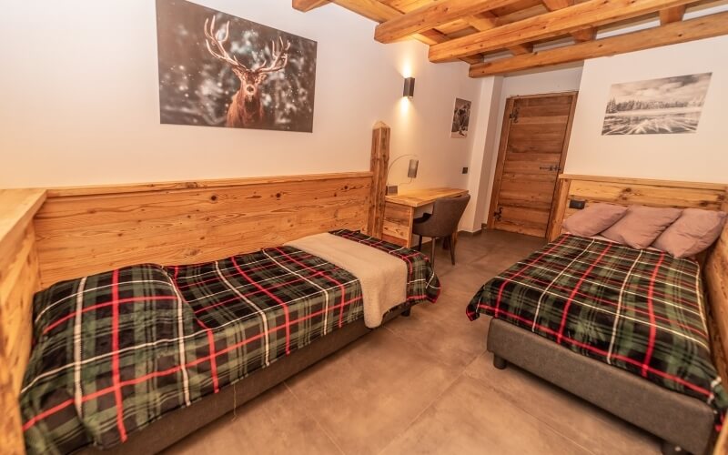Camera accogliente con due letti, scrivania, decorazioni rustiche e pareti bianche, trasmette calore e comfort.