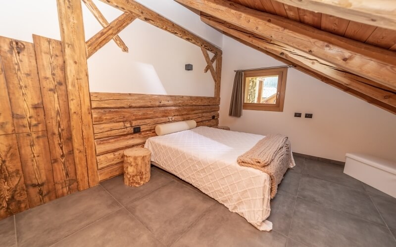 Camera accogliente con letto in legno, coperta bianca, cuscini, finestra con tendina e pavimento in piastrelle.