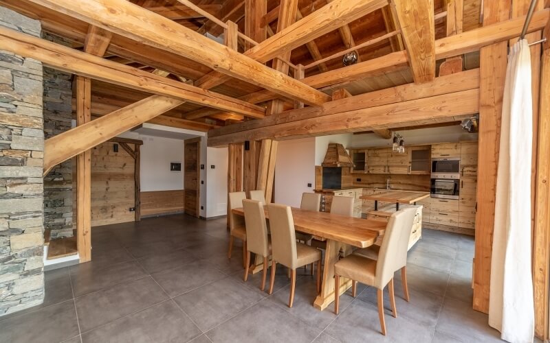 Ampio soggiorno open-space con area pranzo, cucina in legno chiaro e pareti in pietra, atmosfera rustica moderna.