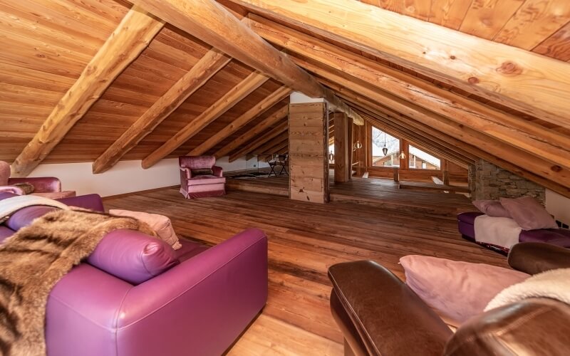 Una spaziosa soffitta con travi a vista, arredamento in pelle sintetica viola e marrone, e luce naturale da una finestra.